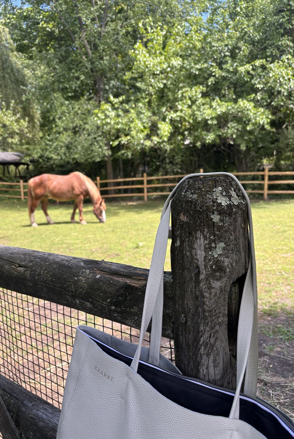 The Essex Tote resting on a wooden fence beside a pasture