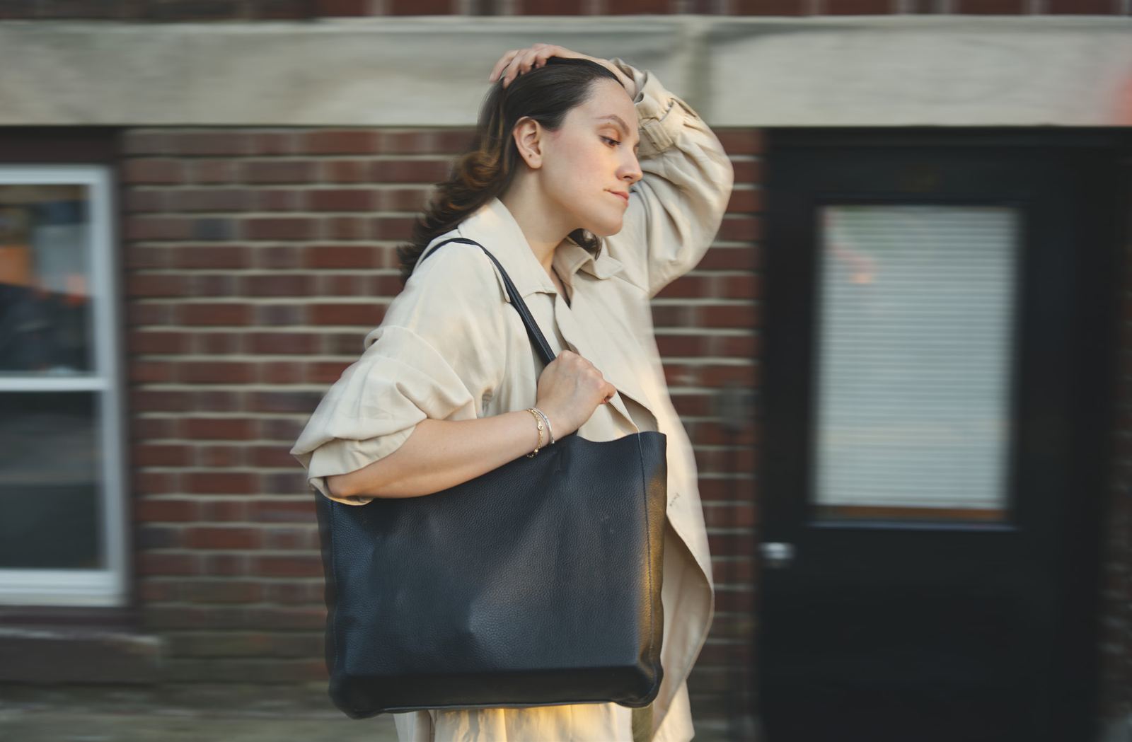 The Essex Tote in noir full-grain leather carried past a brick building